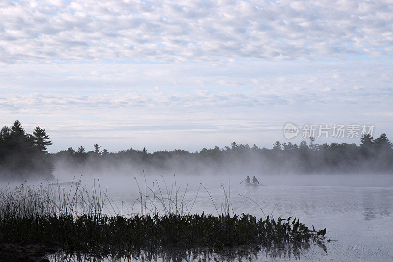 两个人在清晨的薄雾中划独木舟