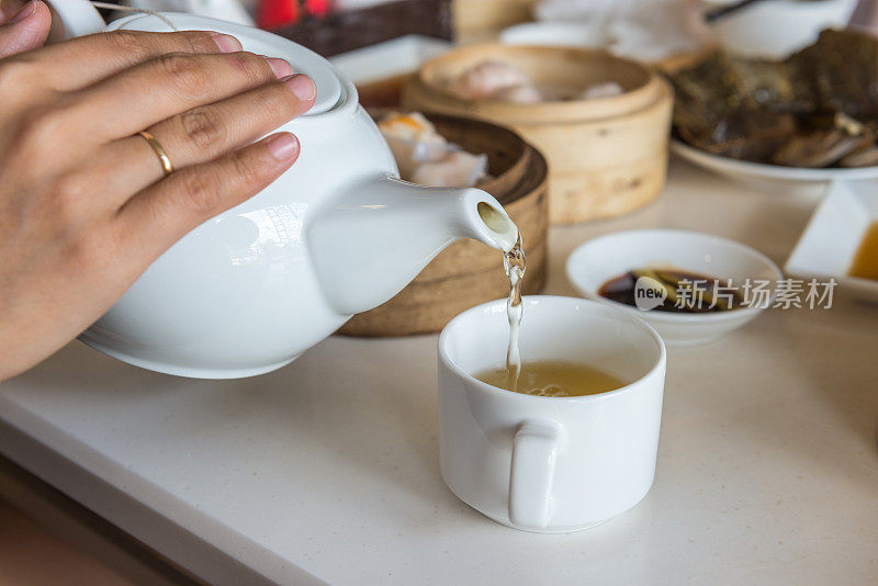 将绿茶从白色茶壶中倒入杯子中
