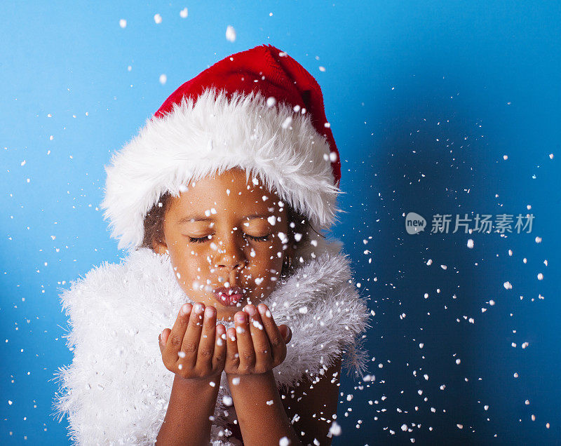 非裔美国小女孩戴着圣诞老人的帽子吹着雪花
