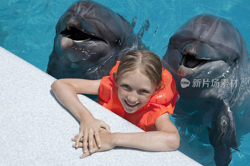快乐的小女孩和两只海豚在游泳池微笑。