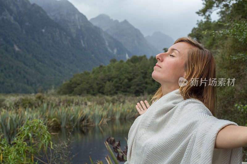 年轻女子在湖边放松的肖像，双臂伸展