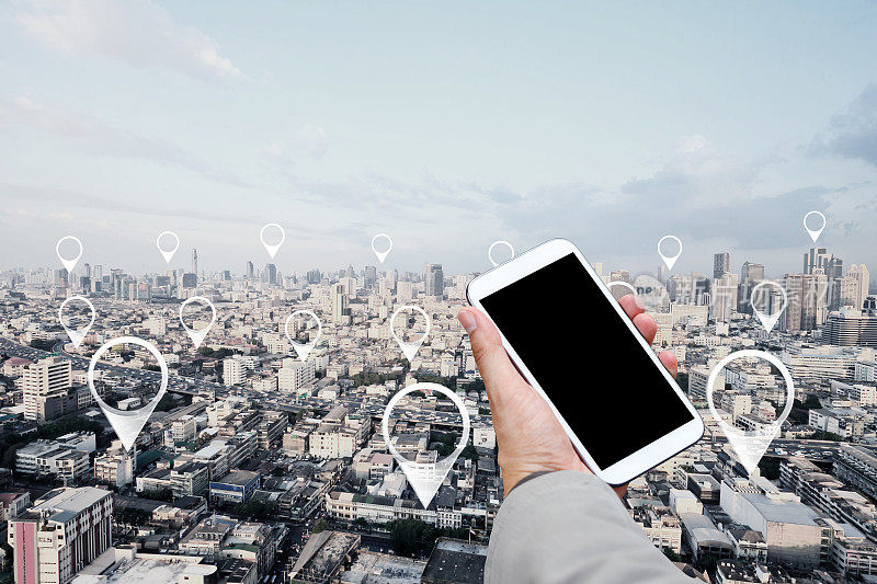 在城市景观和网络连接中使用移动智能手机和地图针的人的手。连接的概念。