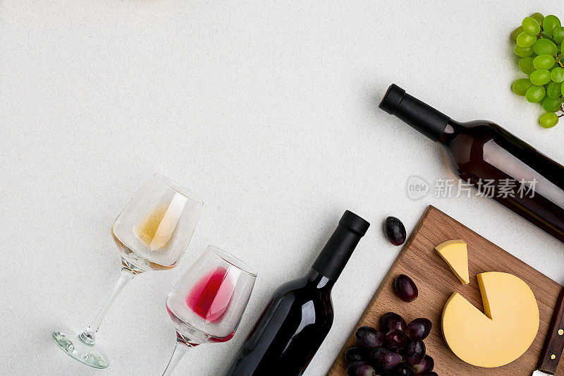 两杯红酒和白酒，一瓶红酒和一瓶白酒，白色背景上的奶酪。从顶部的水平视图