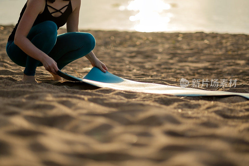 迷人的年轻女子折叠绿色瑜伽或健身垫子后，在海滩上锻炼。