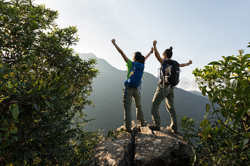 两个年轻的女性成功的背包客享受着悬崖边缘的景色