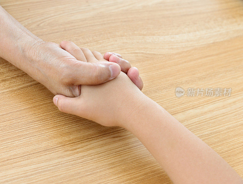 年轻的和年长的妇女手牵着手在木桌的背景上