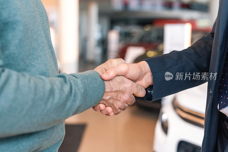 成熟的男人握手与汽车销售员特写。