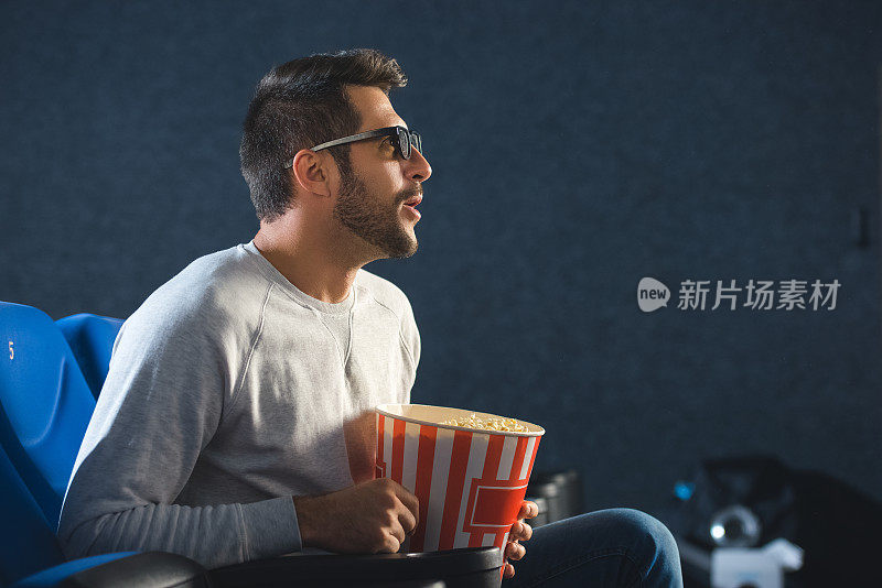 带着3d眼镜和爆米花独自在电影院看电影的情绪化男人的侧视图