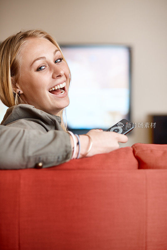 年轻漂亮的金发美女从电视上环顾四周，微笑着，拿着遥控器