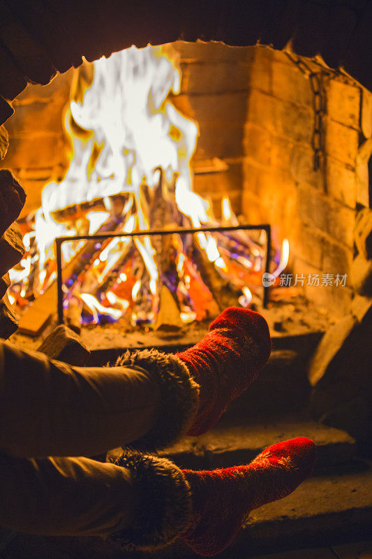 穿着暖袜子的女孩在壁炉边暖腿。冬天可以在壁炉边休息放松。舒适的冬季大气
