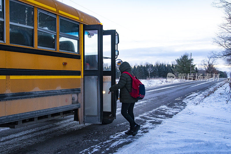 在一个下雪的冬天的早晨，一名青少年在乡村上了一辆校车。
