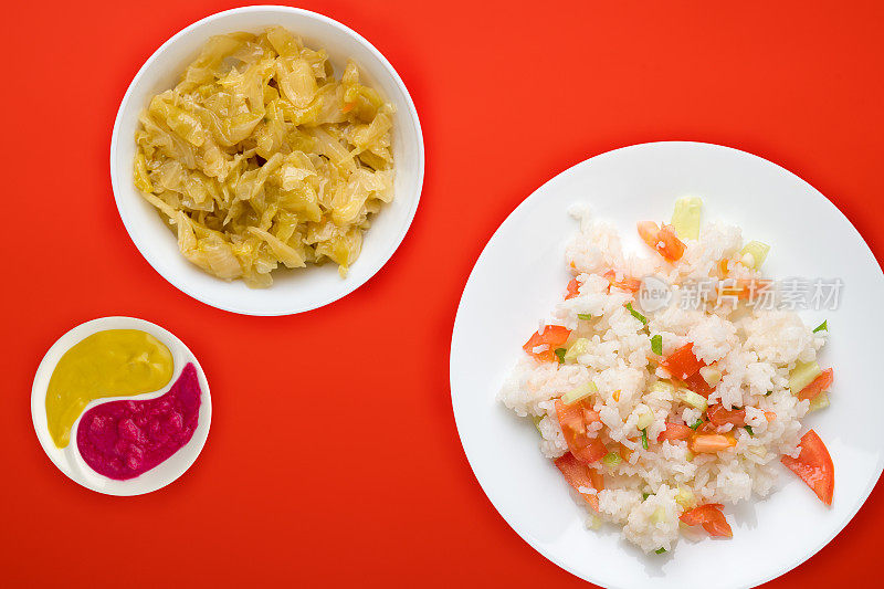 白米饭和蔬菜放在一个白色的盘子上，白米饭和蔬菜沙拉和酱在一个彩色的背景上。米饭配西红柿，黄瓜和洋葱。