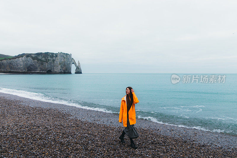 在法国埃特尔塔美丽的海滩上，快乐的女人穿着雨衣散步