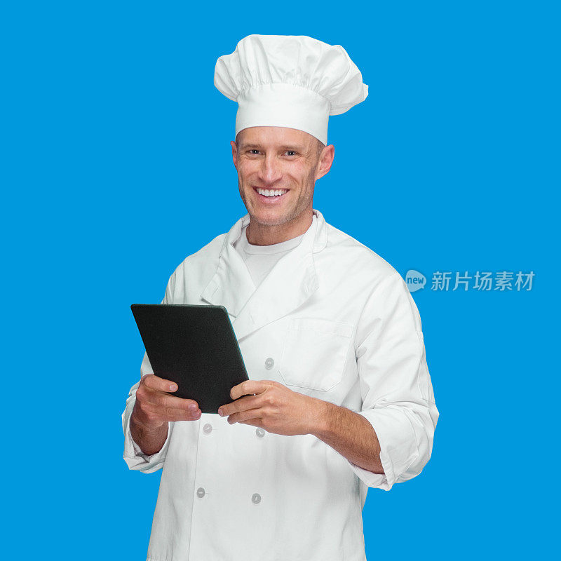 白种年轻男厨师站在蓝色背景下，穿着夹克，使用数码平板电脑