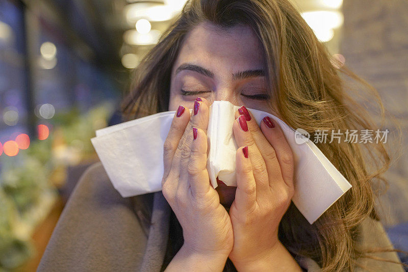 一个生病的年轻女子用纸巾擤鼻子。医疗保健，感冒，过敏和人的概念-生病的妇女在家里用纸巾擤鼻涕