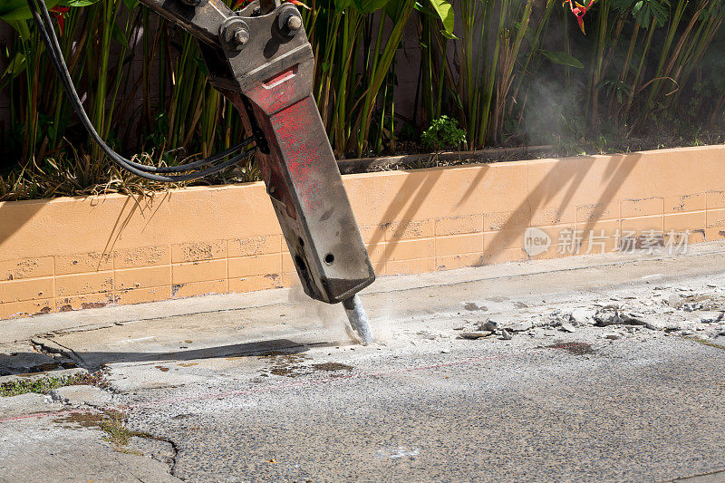 挖掘机破碎钻孔修补混凝土路面。安装在施工设备液压臂上的大型气动锤。施工车辆修路。手提钻钻