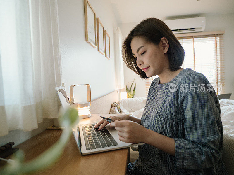 年轻美丽的亚洲女人使用笔记本电脑和信用卡在家里网上购物。