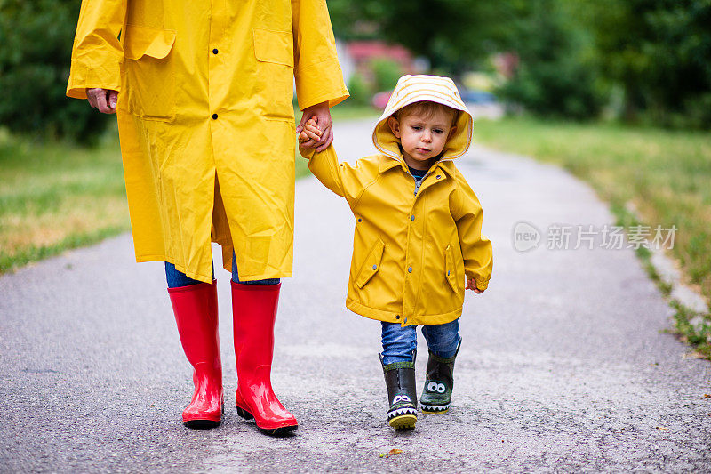 母亲和蹒跚学步的孩子，男孩，在雨中玩耍，穿着靴子和雨衣