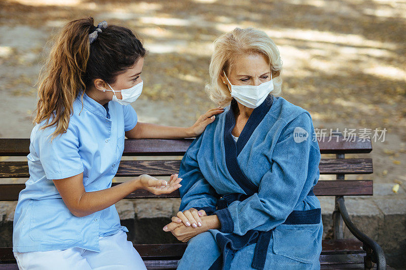 医护人员和戴着防护口罩的年长女性坐在长凳上交流