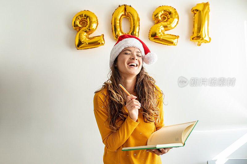 一个微笑的年轻女人的肖像在一个白色的墙壁与圣诞老人的帽子拿着笔记本