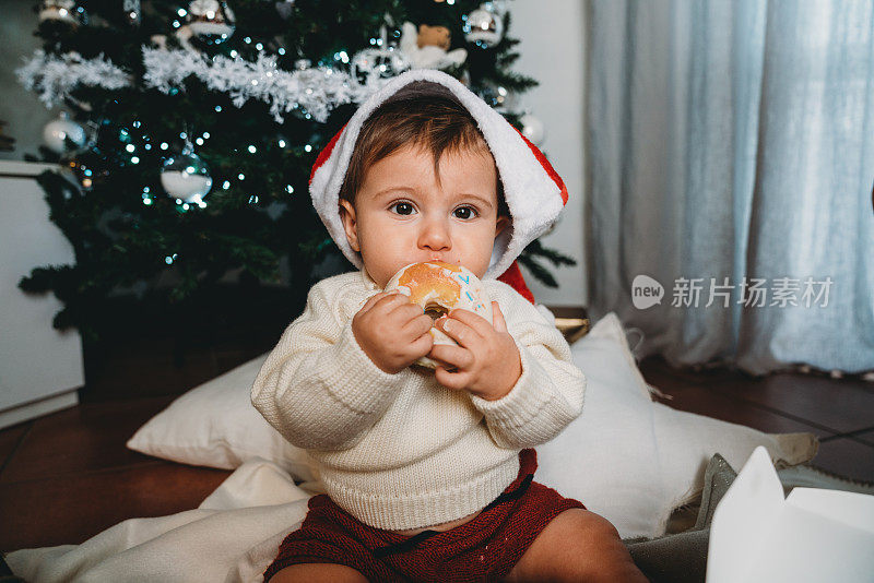 一个小孩正在家里的圣诞树旁吃甜甜圈