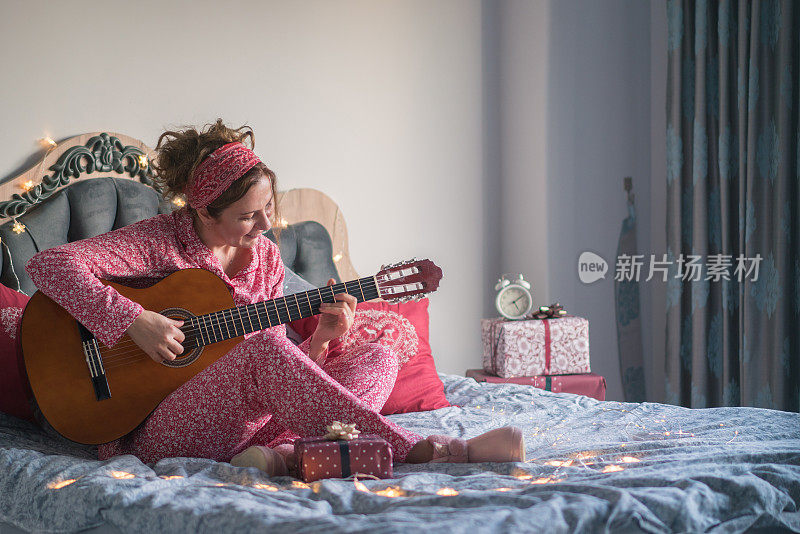 快乐的女人穿着睡衣在床上弹吉他。