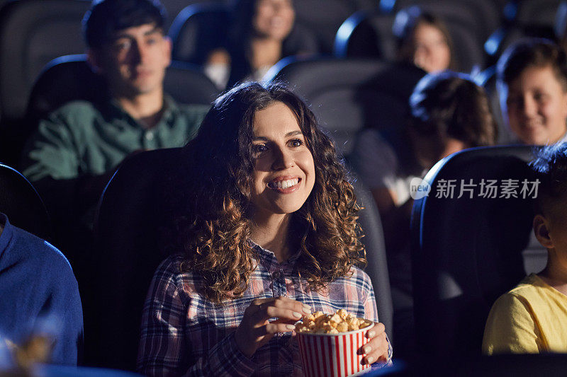 年轻笑着的女人在电影院吃爆米花。