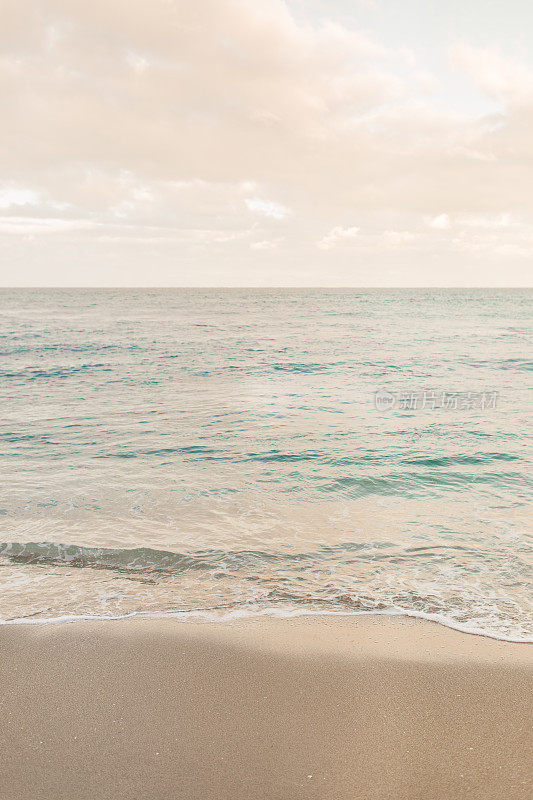 柔和的日落天空在蓝绿色的海浪横扫棕榈滩的海岸线，佛罗里达