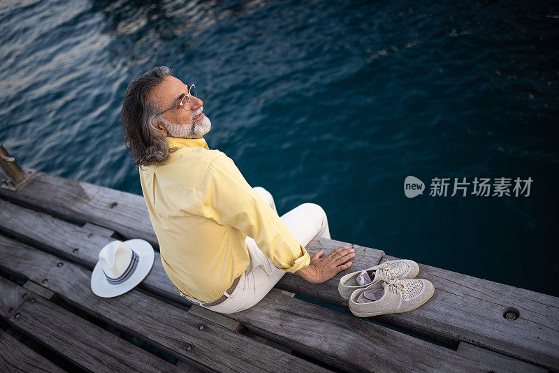 一个成熟的男人坐在木制的码头上，享受海风