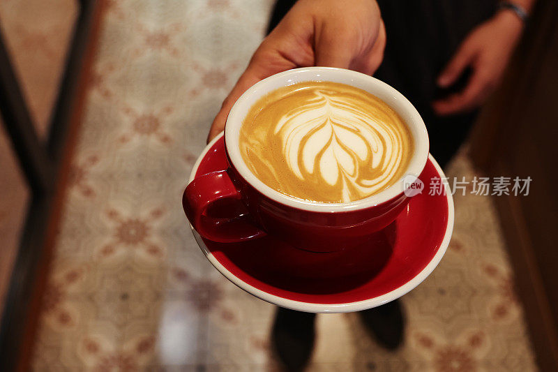咖啡师端上一杯牛奶泡沫上有花图案的拿铁