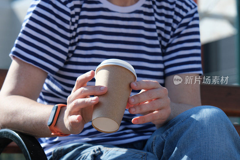 一个人坐在公园长凳上，拿着一次性咖啡杯