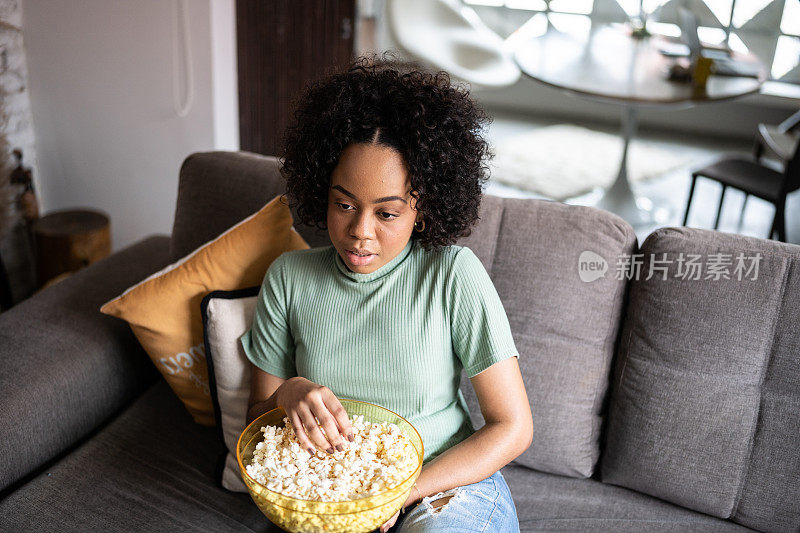 年轻女子在家看电视，吃爆米花