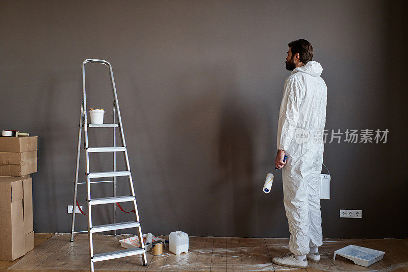 年轻的白人男子穿着防护服在新公寓进行装修工作，准备粉刷墙壁