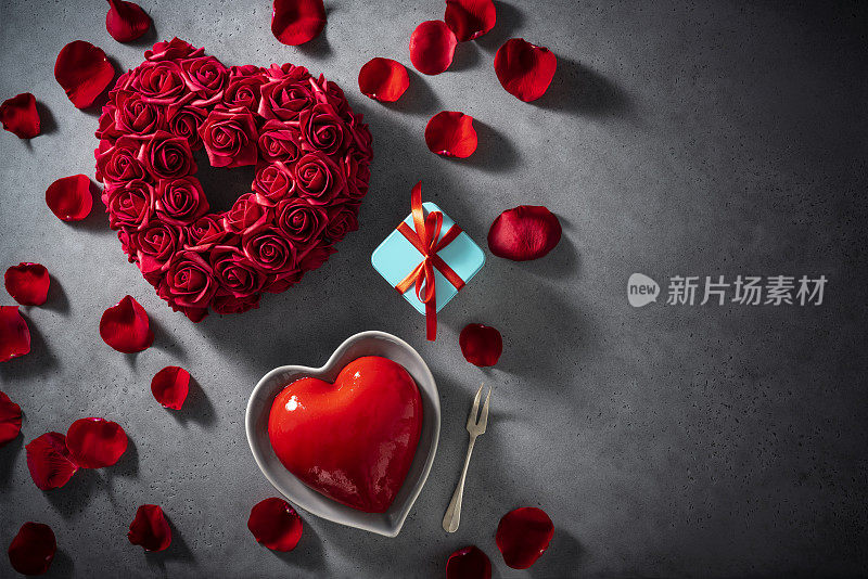 情人节红玫瑰花瓣和心形蛋糕在灰色拷贝空间