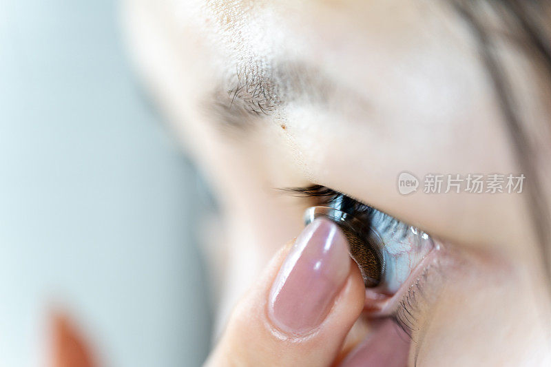 一名年轻的亚洲妇女将一枚棕色隐形眼镜戴在手指上。