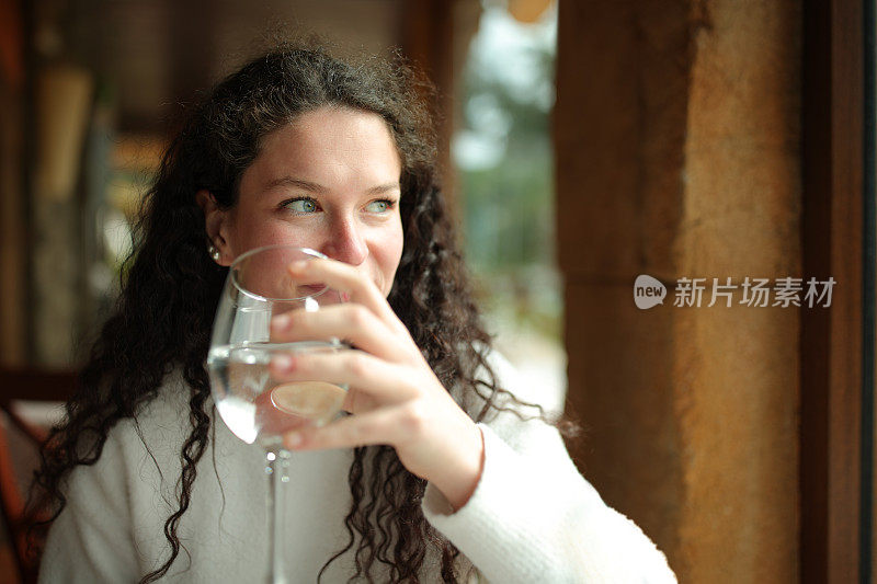 幸福的女人拿着一杯水看着窗外