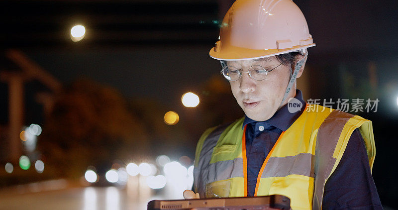 亚洲男性土木工程师或建筑师在立交高速公路施工现场戴安全帽，穿安全背心。夜班工长站在坚固的工业平板上检查结构进度和施工监督。