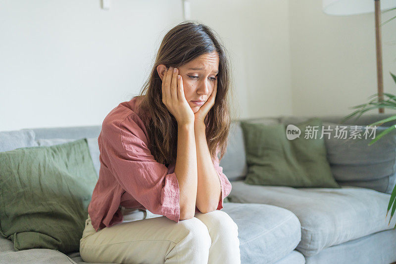 悲伤的年轻女子坐在客厅的沙发上