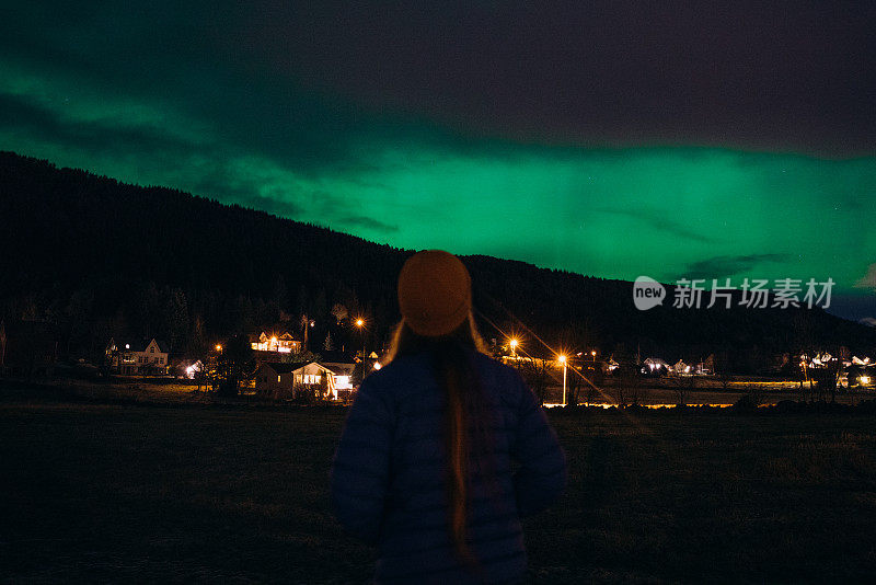 在挪威农村地区，一名女子在天空中欣赏强烈的北极光