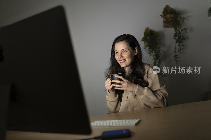 女人坐在办公桌前喝咖啡，用笔记本电脑读电子书，直到深夜