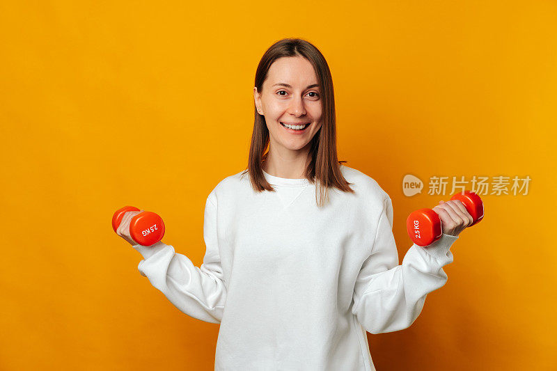 一个拿着两个橙色哑铃微笑着的女人说，做运动，保持健康。