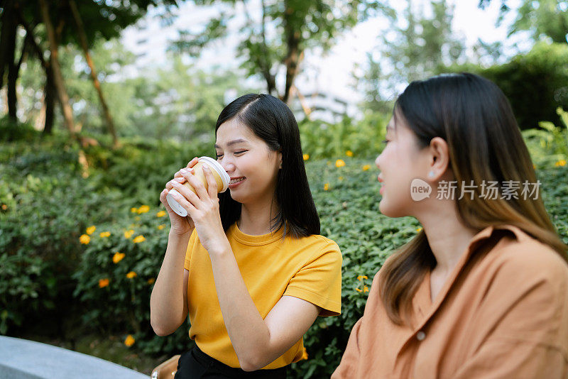 穿着黄色t恤的亚洲妇女在社区花园和朋友闲逛时喝咖啡。