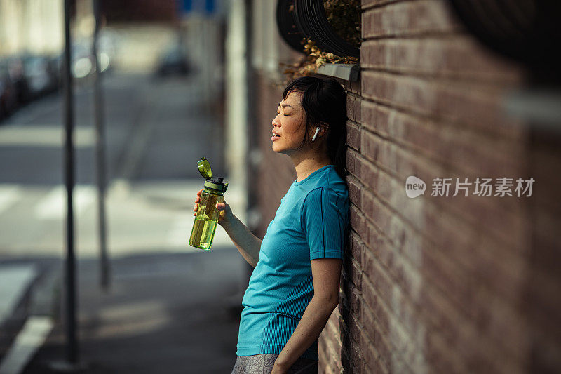 一名年轻的日本女子在城市里运动后休息片刻，喝了点水