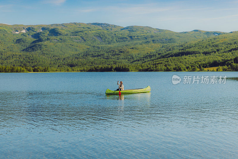 一名女子在挪威风景优美的湖中驾着绿色的独木舟航行