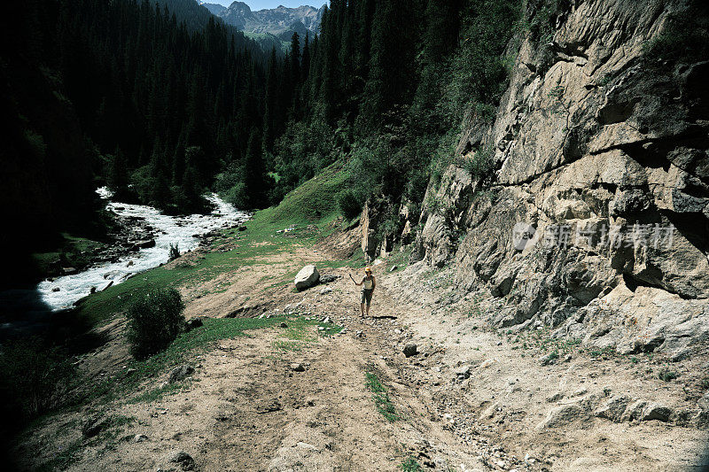 女游客在南天山狭窄峡谷的山河上方的岩石上拍摄视频