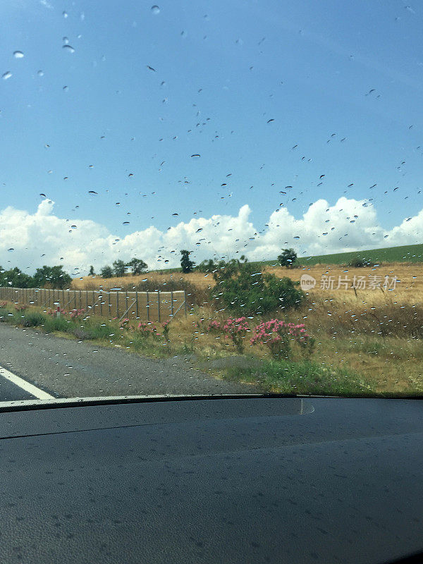 雨点在汽车挡风玻璃上的道路与阳光的自然背景