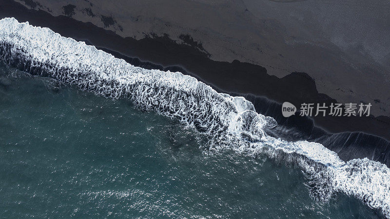 鸟瞰图，海浪拍打着黑色的沙滩，产生了许多海洋泡沫，这是大自然的力量。冰岛