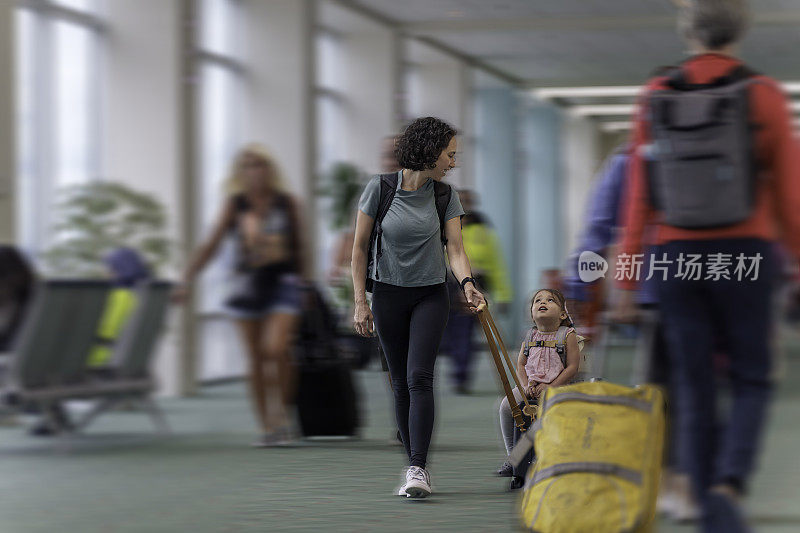 蹒跚学步的小女孩在和妈妈一起旅行时骑着行李箱通过机场