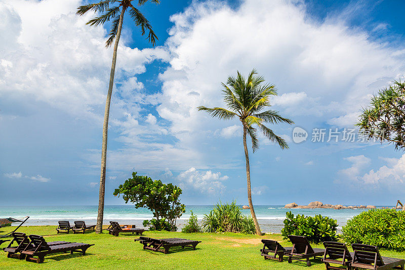 热带海滩度假村在Hikkaduwa与棕榈树，躺椅，和蔚蓝的天空下的海景。