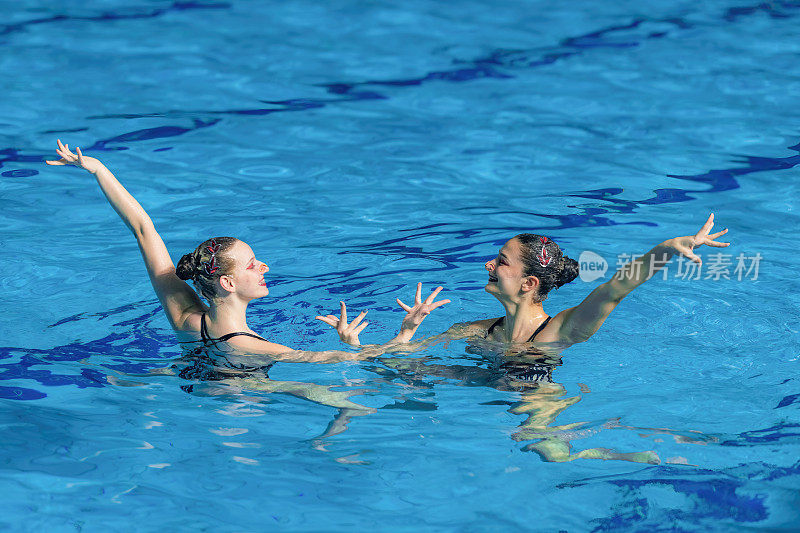 女子双人花样游泳表演，动作流畅，在池中同步优雅